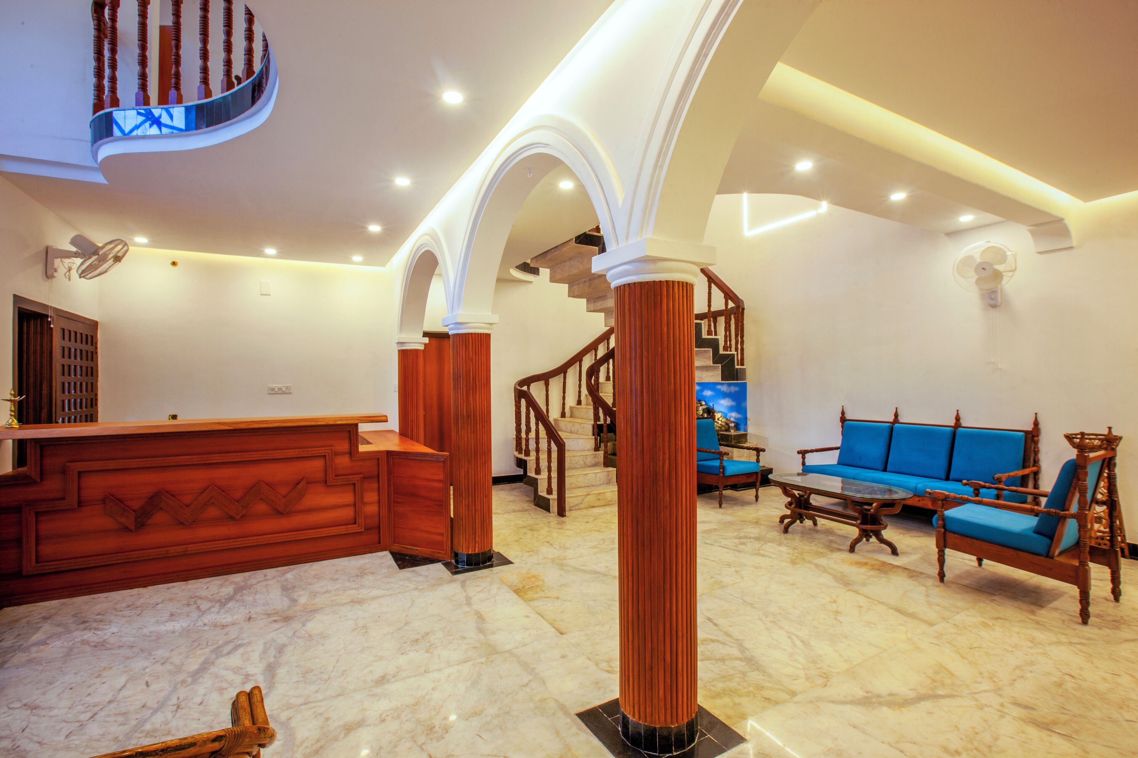 A spacious lobby with a marble floor, a reception desk, a staircase, and a blue sofa.