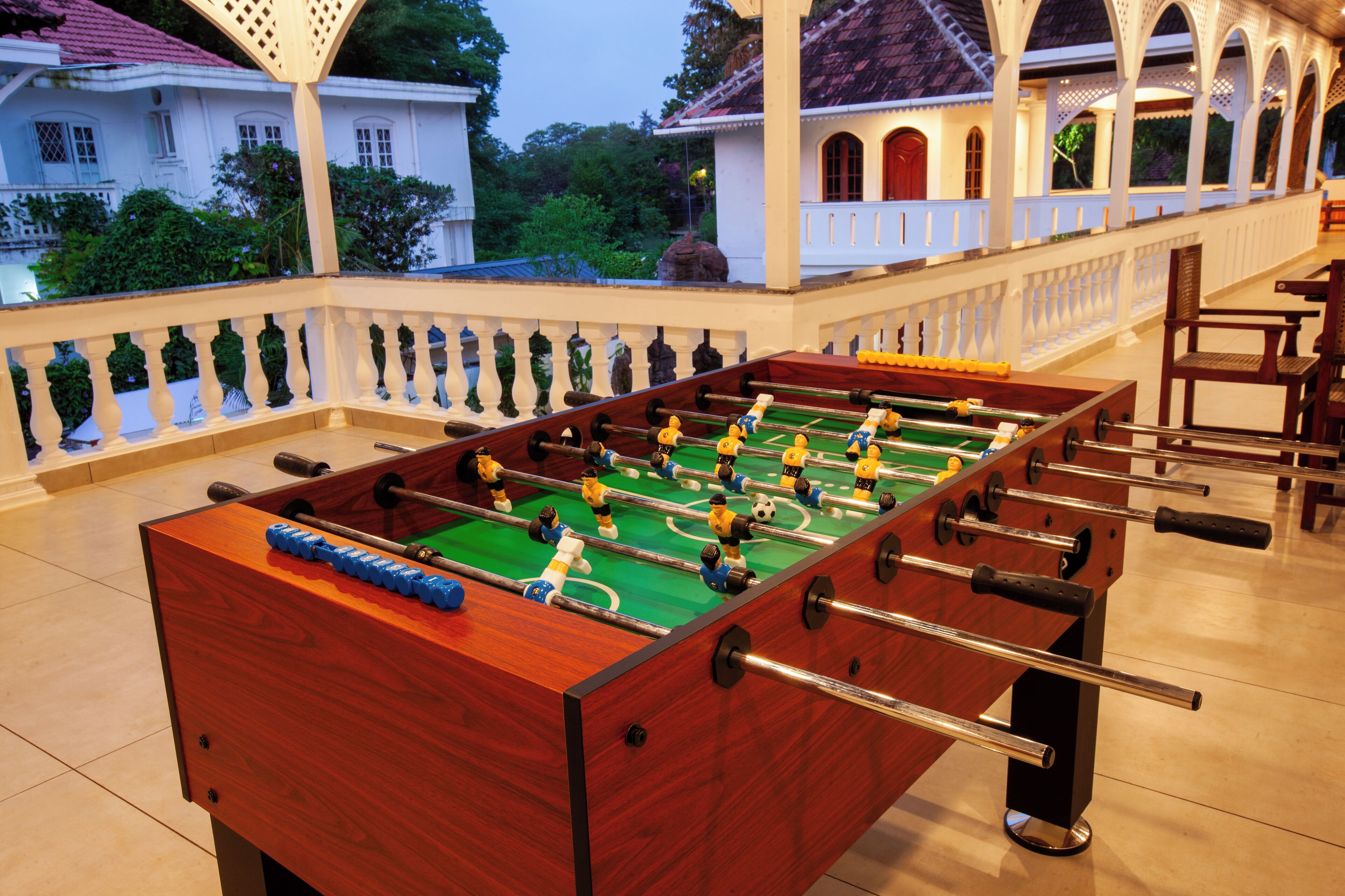 A foosball table in a well-lit indoor area with a view of a white building and greenery outside.
