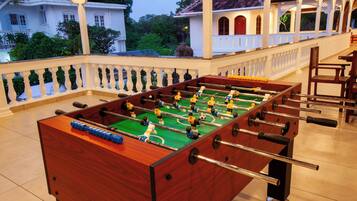 A foosball table in a well-lit indoor area with a view of a white building and greenery outside.