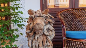 A wooden lion sculpture on a black marble floor next to a wicker chair with a blue cushion. - Villa Elixir Fort Kochi (Kochi)