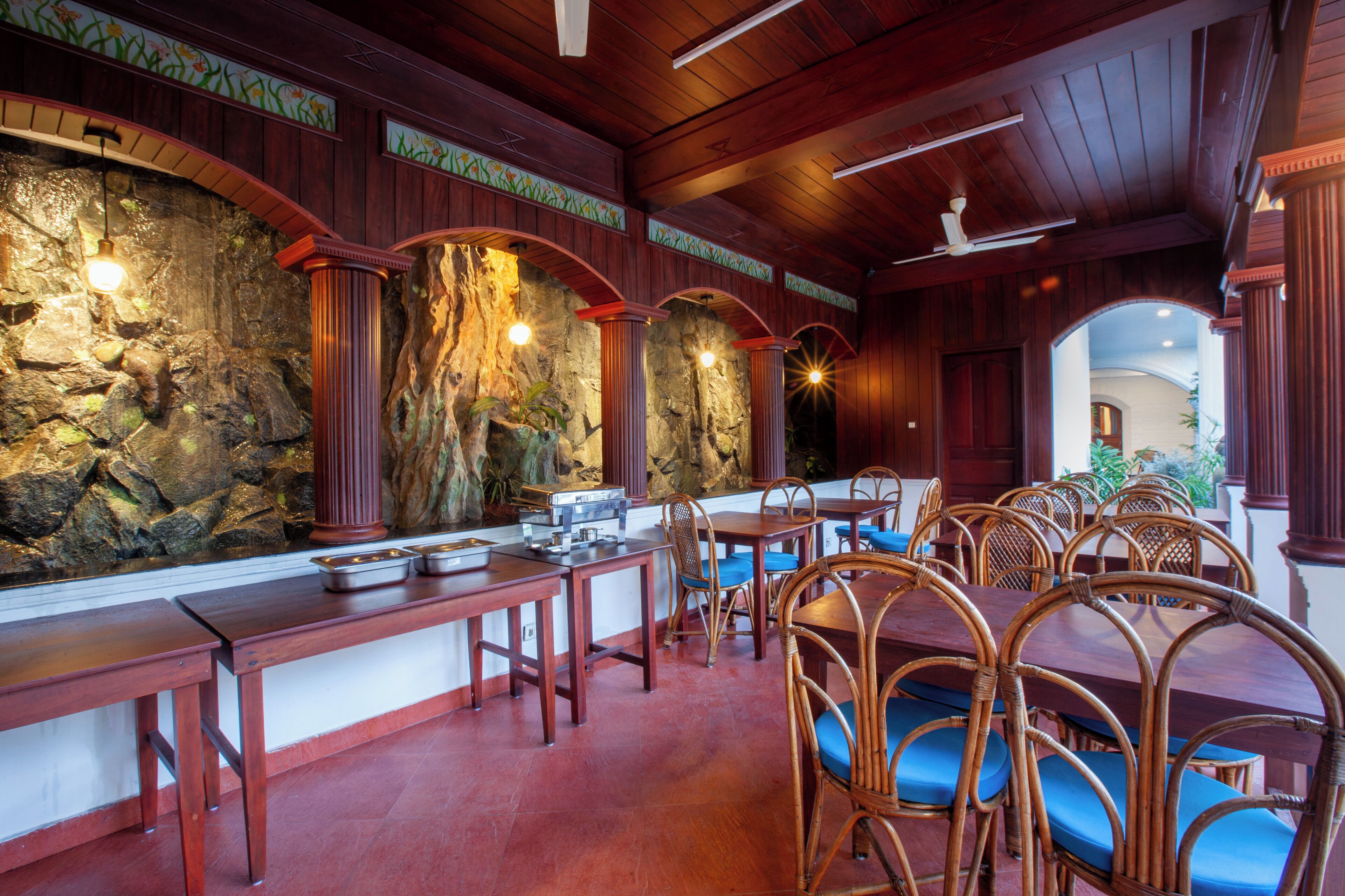 A restaurant with wooden tables and chairs, a stone wall, and a ceiling fan.