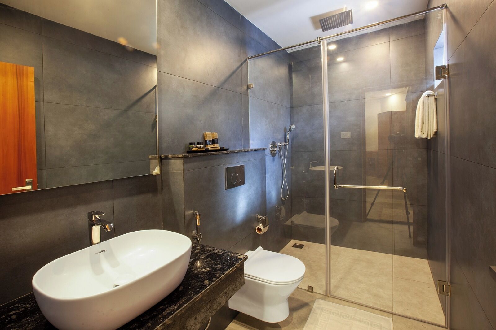 Un baño moderno con un lavamanos grande de color blanco, un inodoro y una zona de ducha con mampara de vidrio.