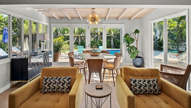 A sunlit room with a pool view, featuring a dining table, two sofas, and a ceiling fan. - Mid-Century Oasis | Resort Backyard | Near Beach (Fort Lauderdale)