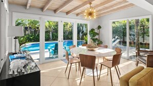 A spacious indoor area with a pool view, a round table with chairs, and a ceiling with exposed beams. - Mid-Century Oasis | Resort Backyard | Near Beach (Fort Lauderdale)