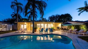 A poolside area with lounge chairs, a barbecue, and a building with doors and windows. - Mid-Century Oasis | Resort Backyard | Near Beach (Fort Lauderdale)