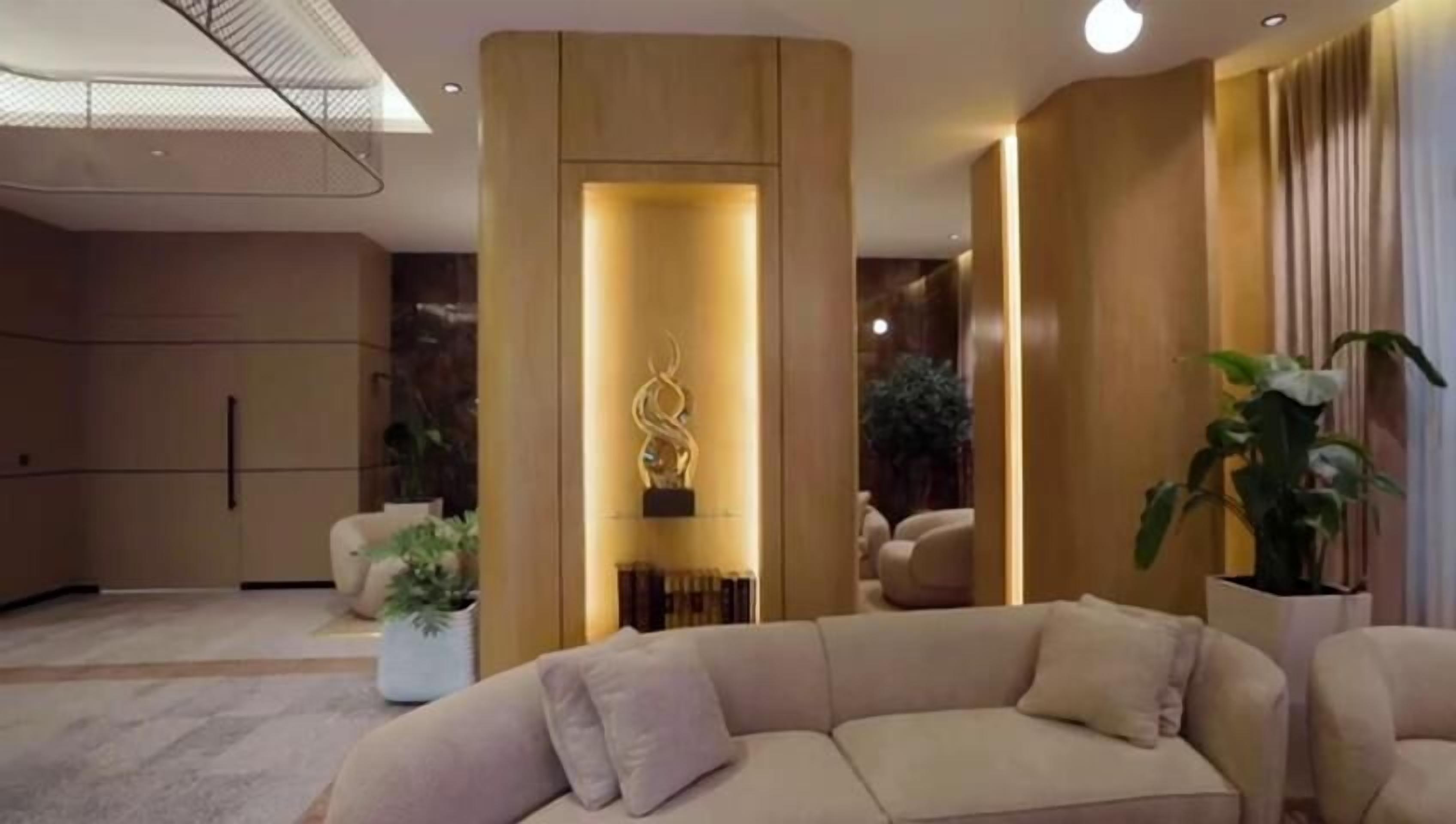 A modern living room with a beige sofa, a decorative wall piece, and potted plants.