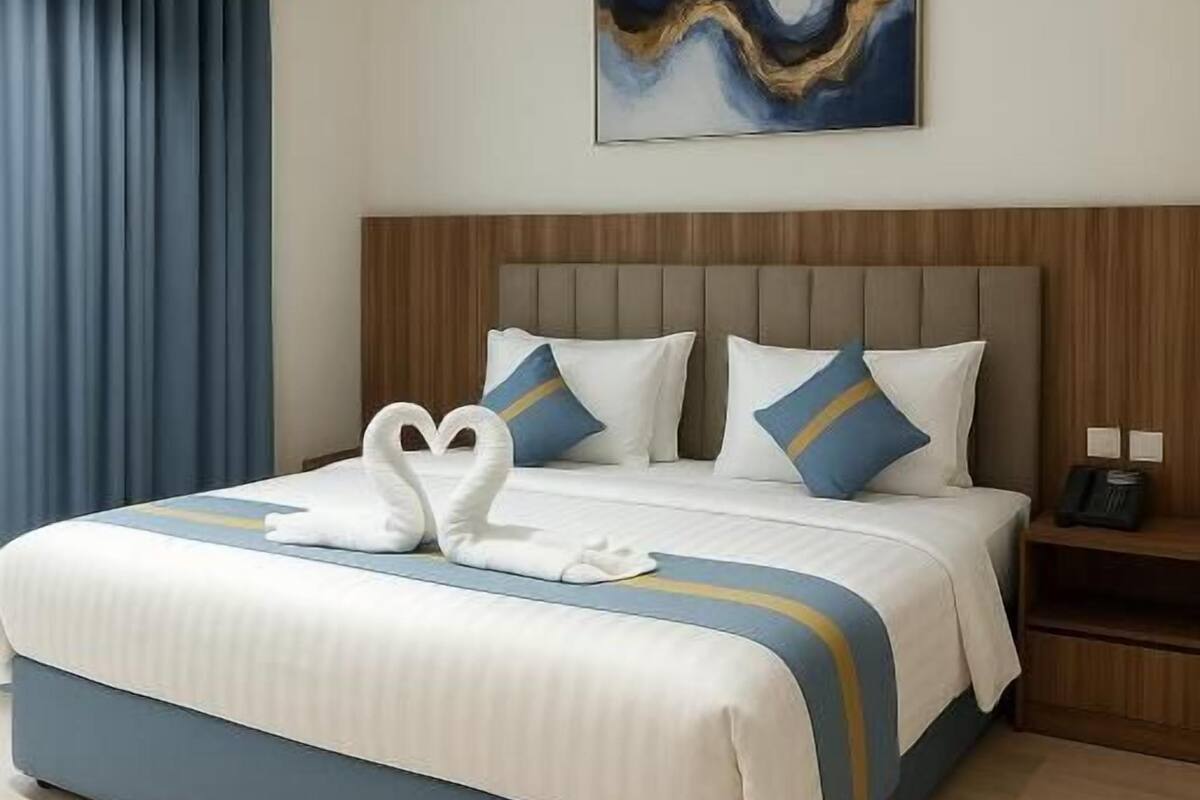 A hotel room with a large bed, a wooden headboard, and a painting on the wall.