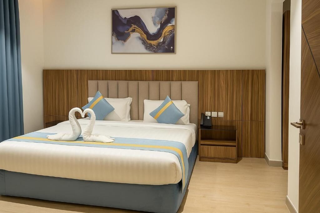 A hotel room with a large bed, a wooden headboard, a nightstand, and a painting on the wall.