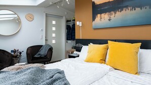 A modern bedroom with a skylight, a large bed with yellow pillows, a round mirror, and a painting of a landscape. - Ice and light village (Luleå)
