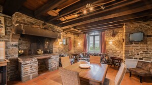A rustic dining area with stone walls, wooden beams, and wicker furniture. - Holiday Home Château de Boucéel Mont Saint Michel (Saint-James)