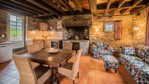 A rustic kitchen with stone walls, wooden beams, and a dining area with wicker chairs and a wooden table. - Holiday Home Château de Boucéel Mont Saint Michel (Saint-James)