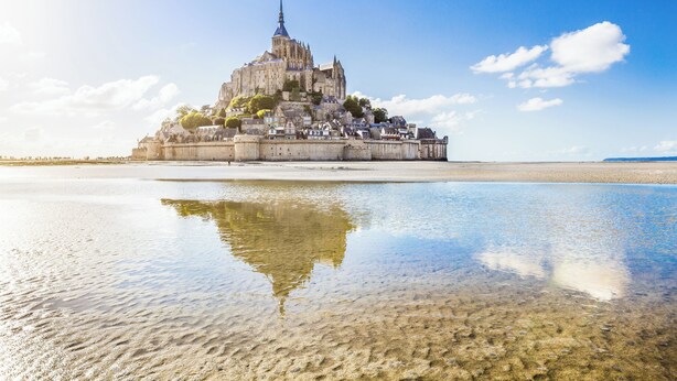 A historic cathedral with a prominent spire, situated on a coastal bluff overlooking a calm body of water. - Holiday Home Château de Boucéel Mont Saint Michel (Saint-James)