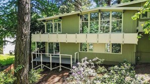 A two-story building with a flat roof and large windows, surrounded by trees and a garden.