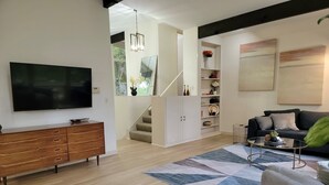 A modern living room with a flat-screen TV, wooden cabinet, staircase, and a sofa.