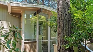 A small, single-story building with a glass door and windows, surrounded by trees.