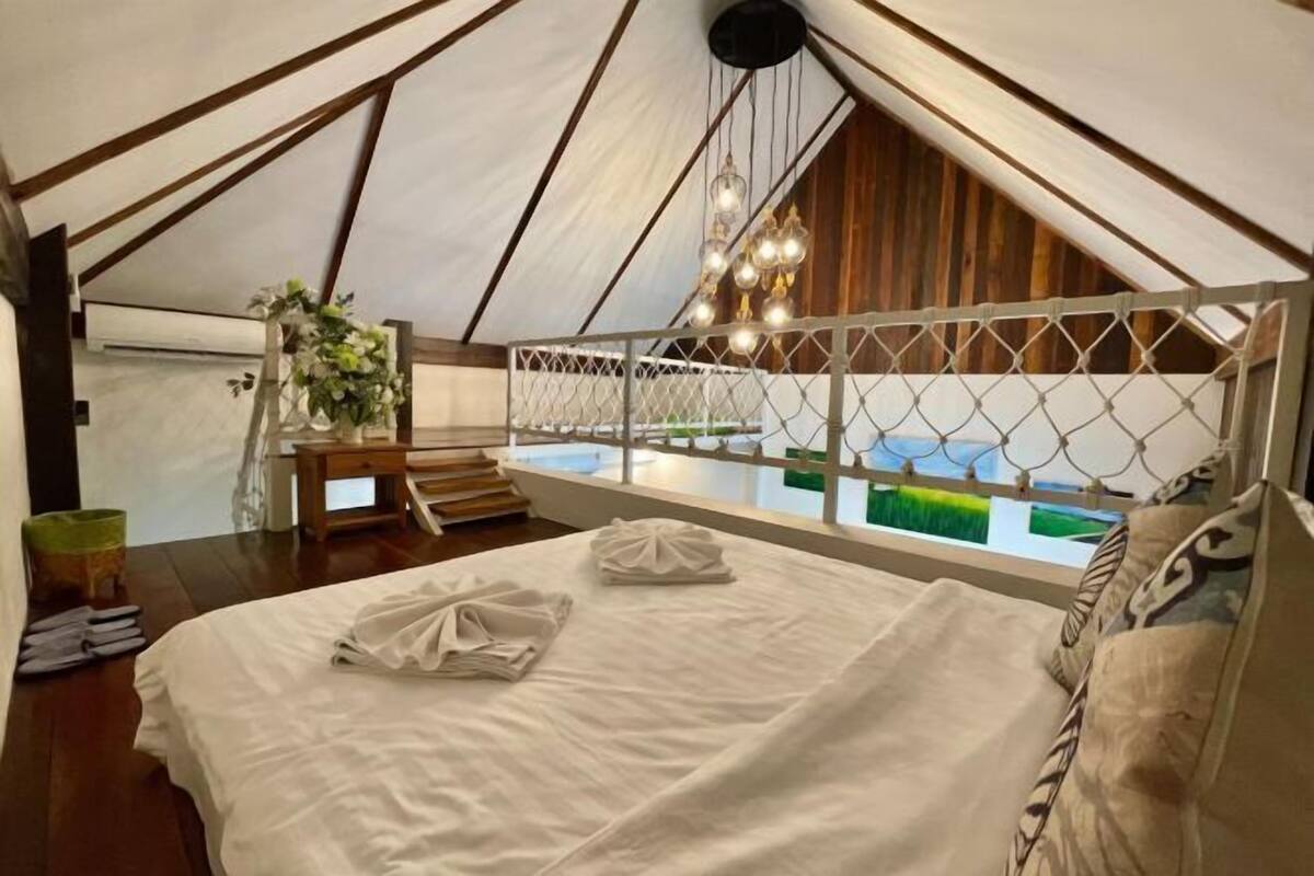 A tented accommodation with a bed, a view of greenery, and a hanging light fixture.