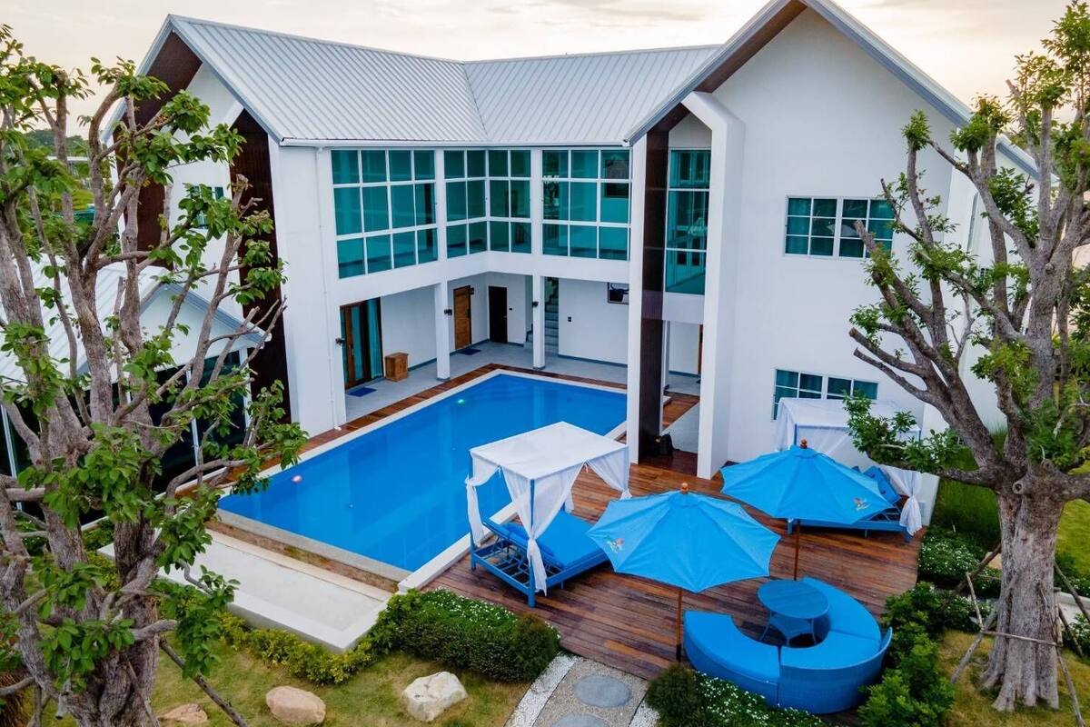 A modern two-story house with a large swimming pool, outdoor seating, and a well-maintained garden.