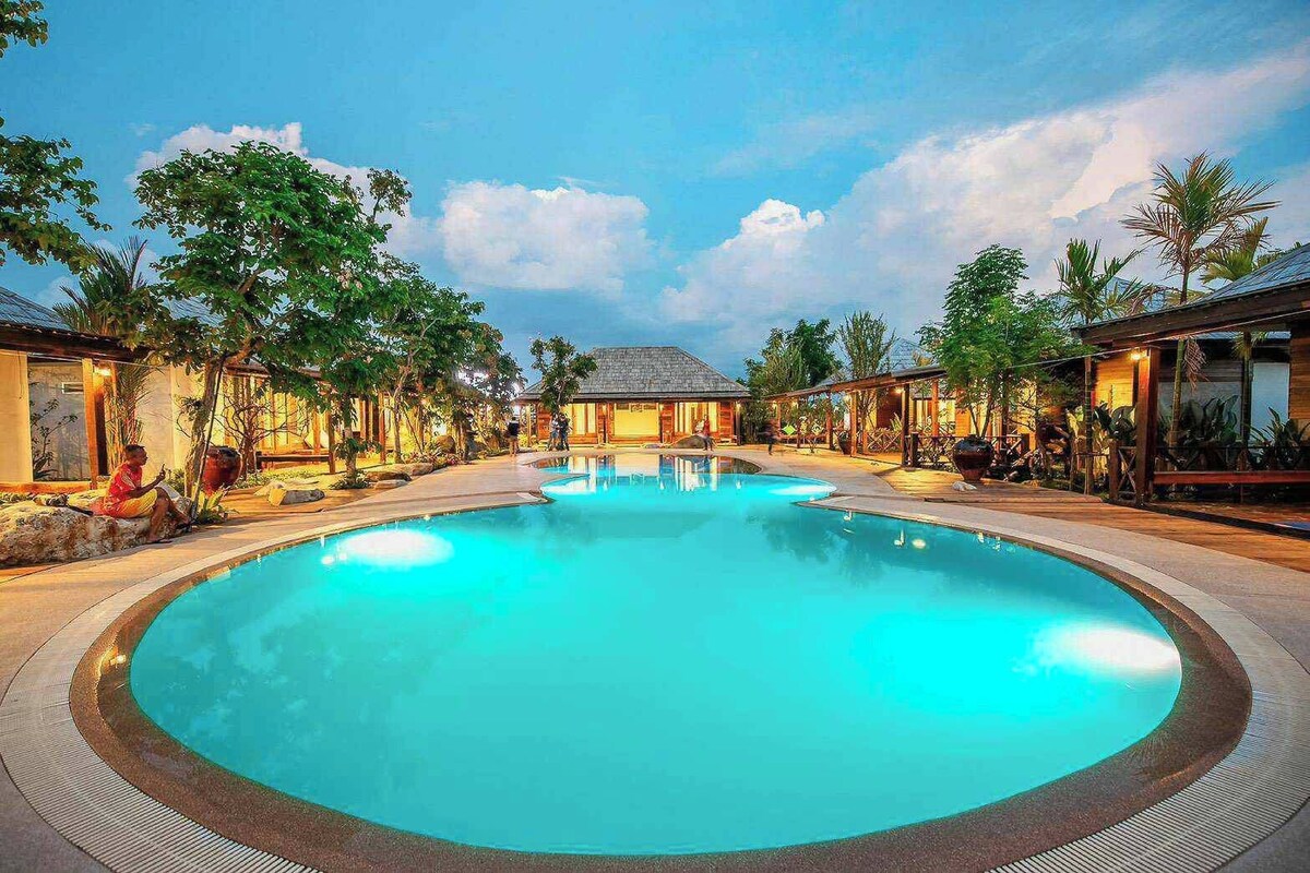 A large outdoor swimming pool surrounded by buildings with a tropical setting.