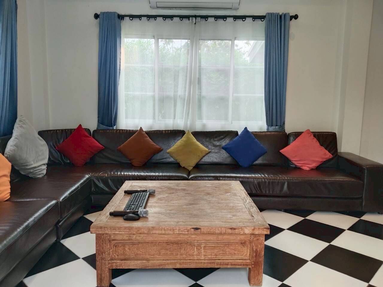 Een woonkamer met een zwart-wit geruite vloer, een houten salontafel en een bruine leren bank met kleurrijke kussens.