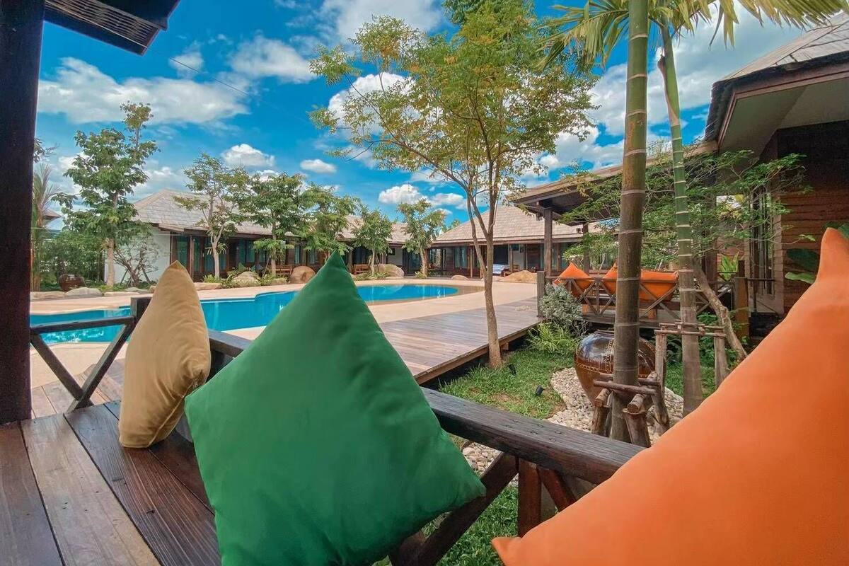A wooden deck with a pool, surrounded by tropical trees and a clear sky.