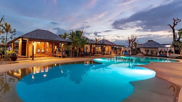 A resort with a large swimming pool, wooden cabins, and tropical landscaping. - Buffalo Island Resort & Adventure Park (Hang Dong)