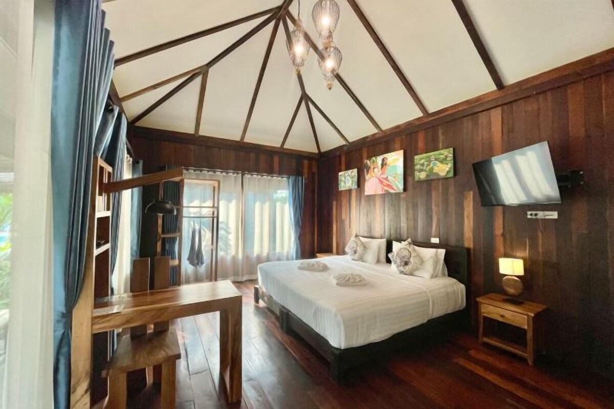 Quarto com uma cama grande, paredes de madeira, uma escrivaninha e uma televisão.