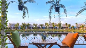 A wooden deck with two chairs and a table overlooking a pool and a row of villas. - Buffalo Island Resort & Adventure Park (Hang Dong)