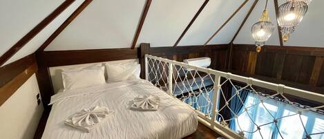 A bedroom with a wooden ceiling, a bed with white linens, a hanging light fixture, and a view through a window with curtains.
