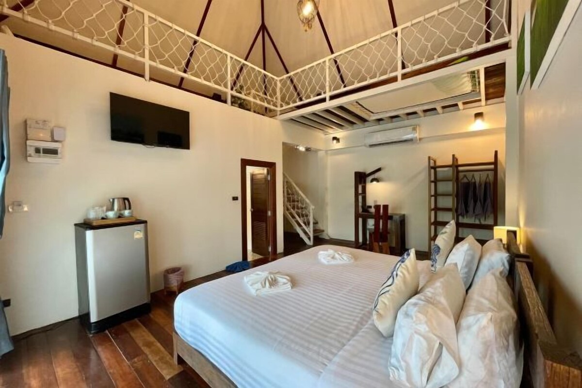A bedroom with a bed, a small refrigerator, a staircase, and a wardrobe.