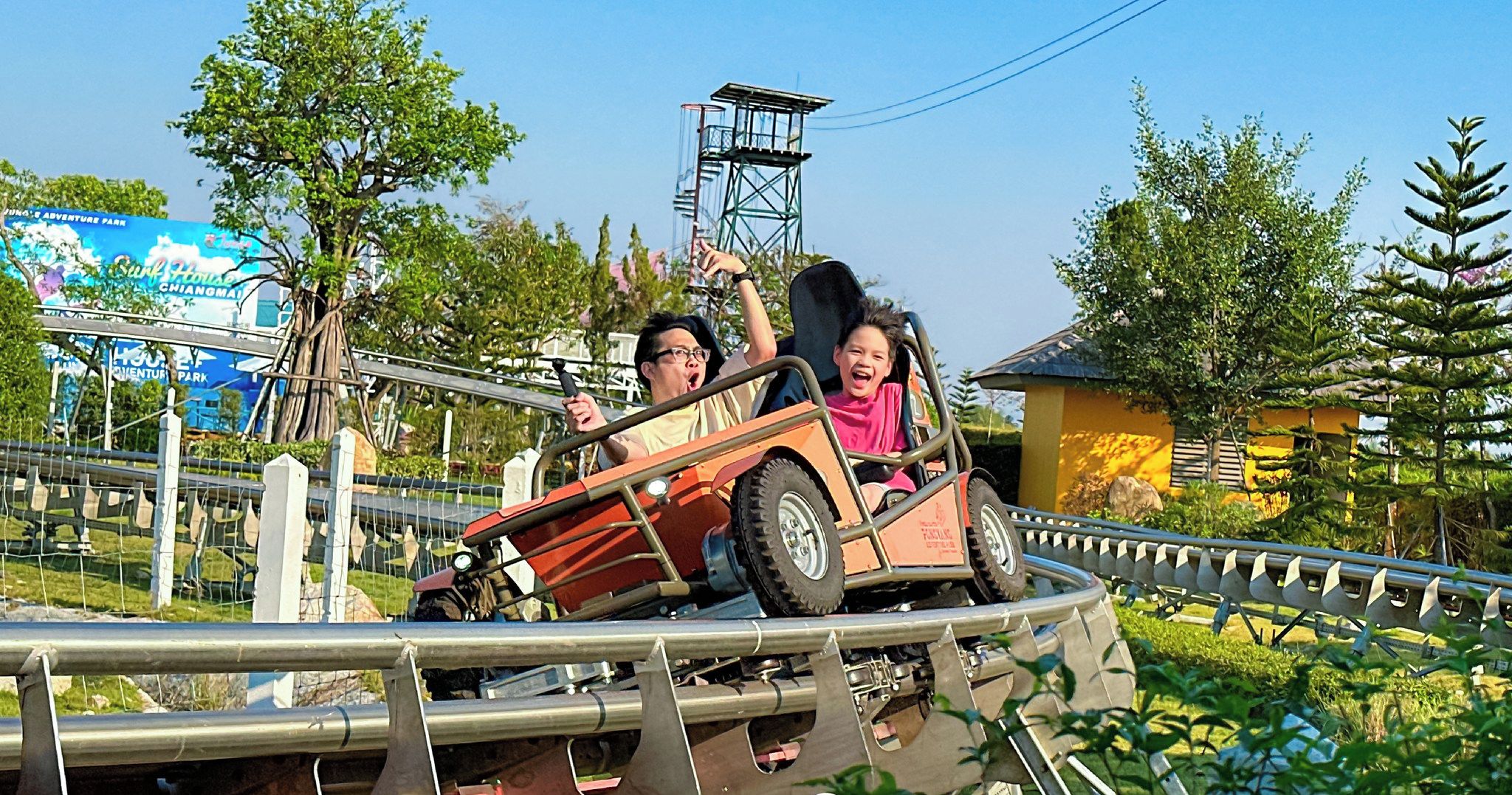 Un petit train de montagnes russes avec deux passagers, entouré de verdure et circulant sur les rails d’une montagne russe.