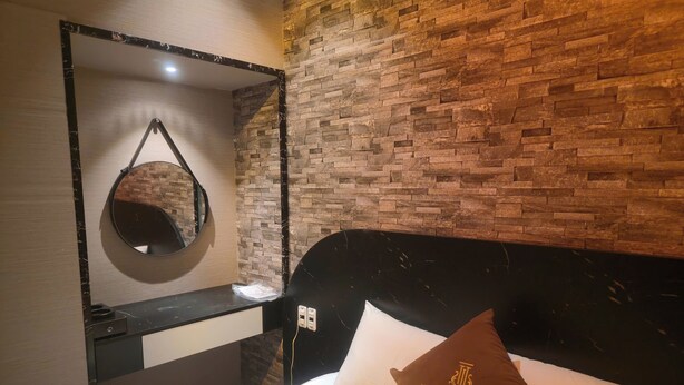 Ein Hotelzimmer mit Backsteinwand, einem runden Spiegel, einem schwarzen Kopfteil und einem Bett mit einem Kissen mit der Aufschrift 'NP LUXURY MOTEL'.