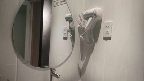 Ein Badezimmer mit einem schwarzen Waschbecken, einem runden Spiegel und einem an der Wand befestigten Föhn.