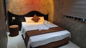 Ein Hotelzimmer mit Bett, einem Kopfkissen mit Logo, einem Nachttisch und einer Wand mit strukturierter Oberfläche.