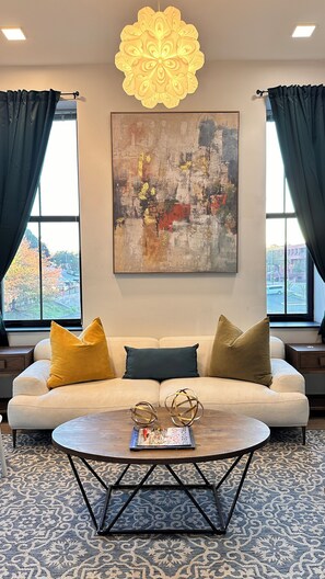 Sala de estar com sofá, almofadas, mesa de centro, luminária decorativa e um quadro na parede.