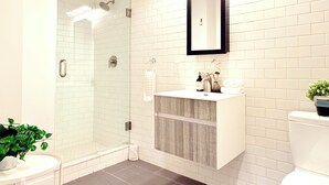 A modern bathroom with a glass shower, white subway tiles, a wooden vanity, and a white toilet.