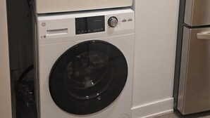 A stacked washer and dryer unit with a control panel, a power cord, and a detergent bottle on top.