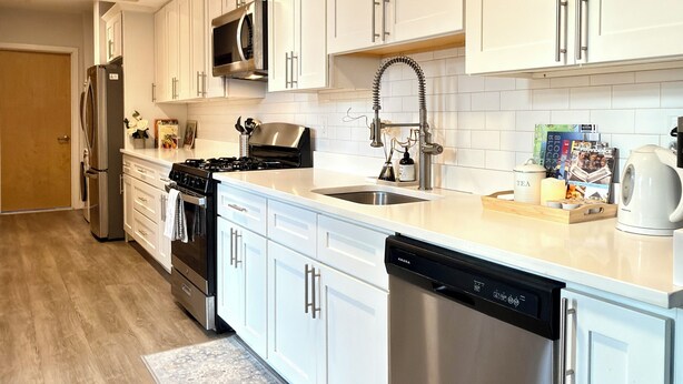 A modern kitchen with white cabinets, stainless steel appliances, and a wooden ceiling.
