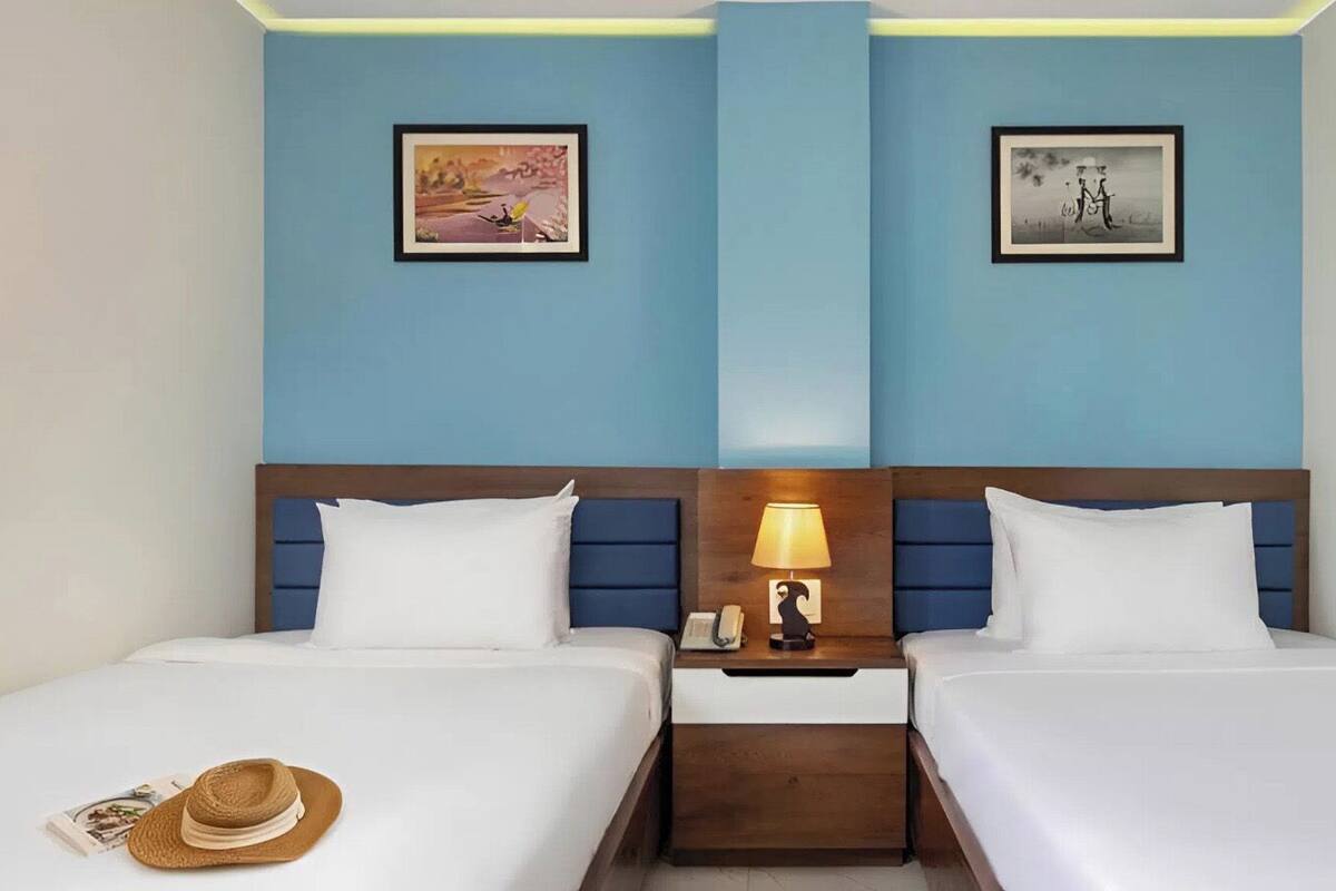 Una habitación de hotel con dos camas, una mesita de noche con lámpara y obras de arte en las paredes.