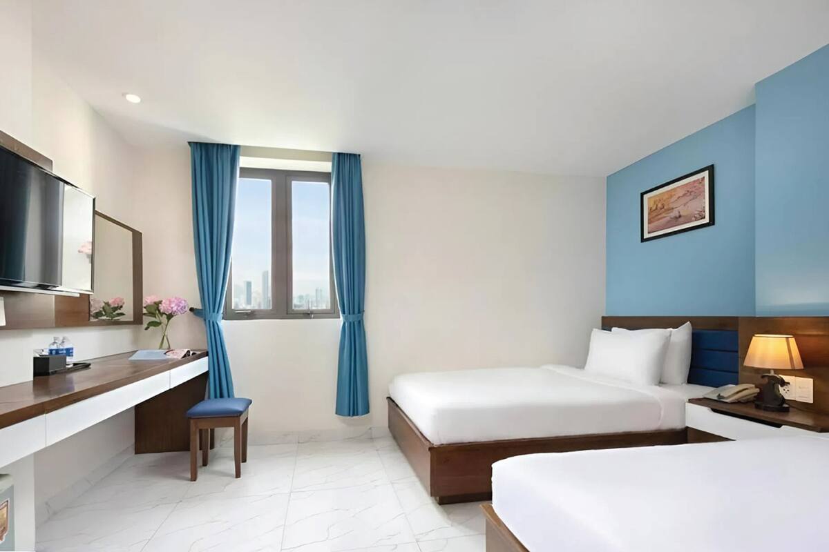 Una habitación de hotel con cama, escritorio, silla y ventana con cortinas.