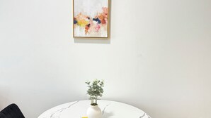 Une table de salle à manger ronde, surmontée d’un plateau en marbre blanc, est entourée de deux chaises noires à revêtement rembourré. Un vase blanc contenant des plantes vertes est posé sur la table.