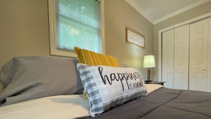 Un lit bien fait, avec un coussin orné de l’inscription : « Le bonheur, c’est chez soi. »