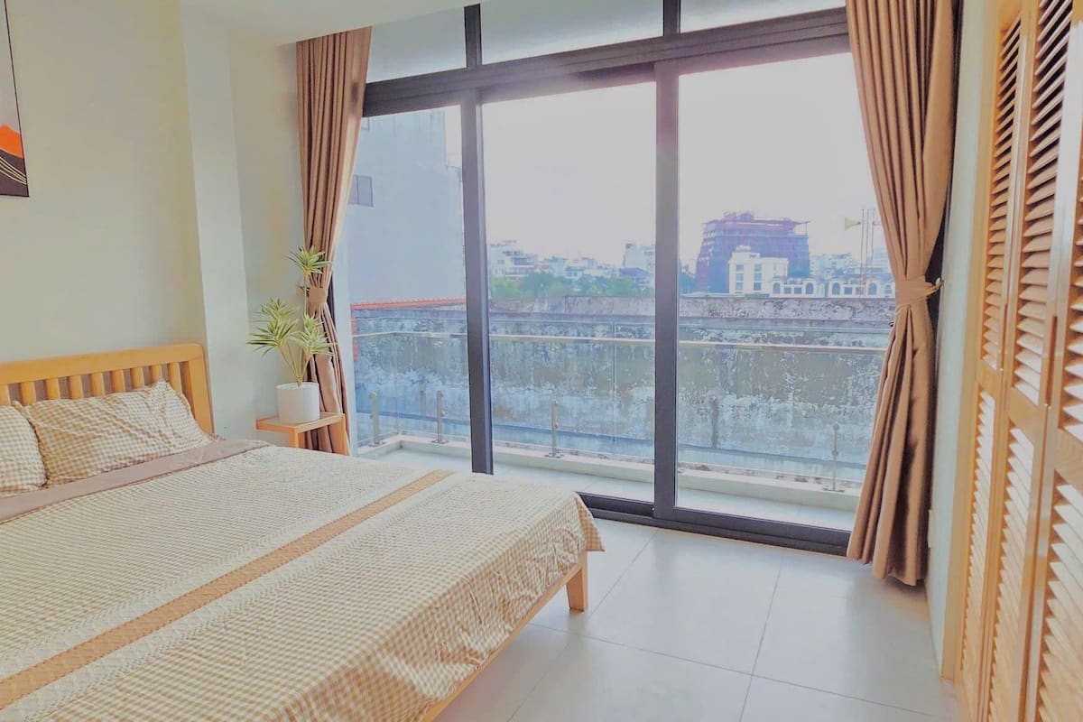 A bedroom with a large bed, a window with curtains, and a view of a cityscape.