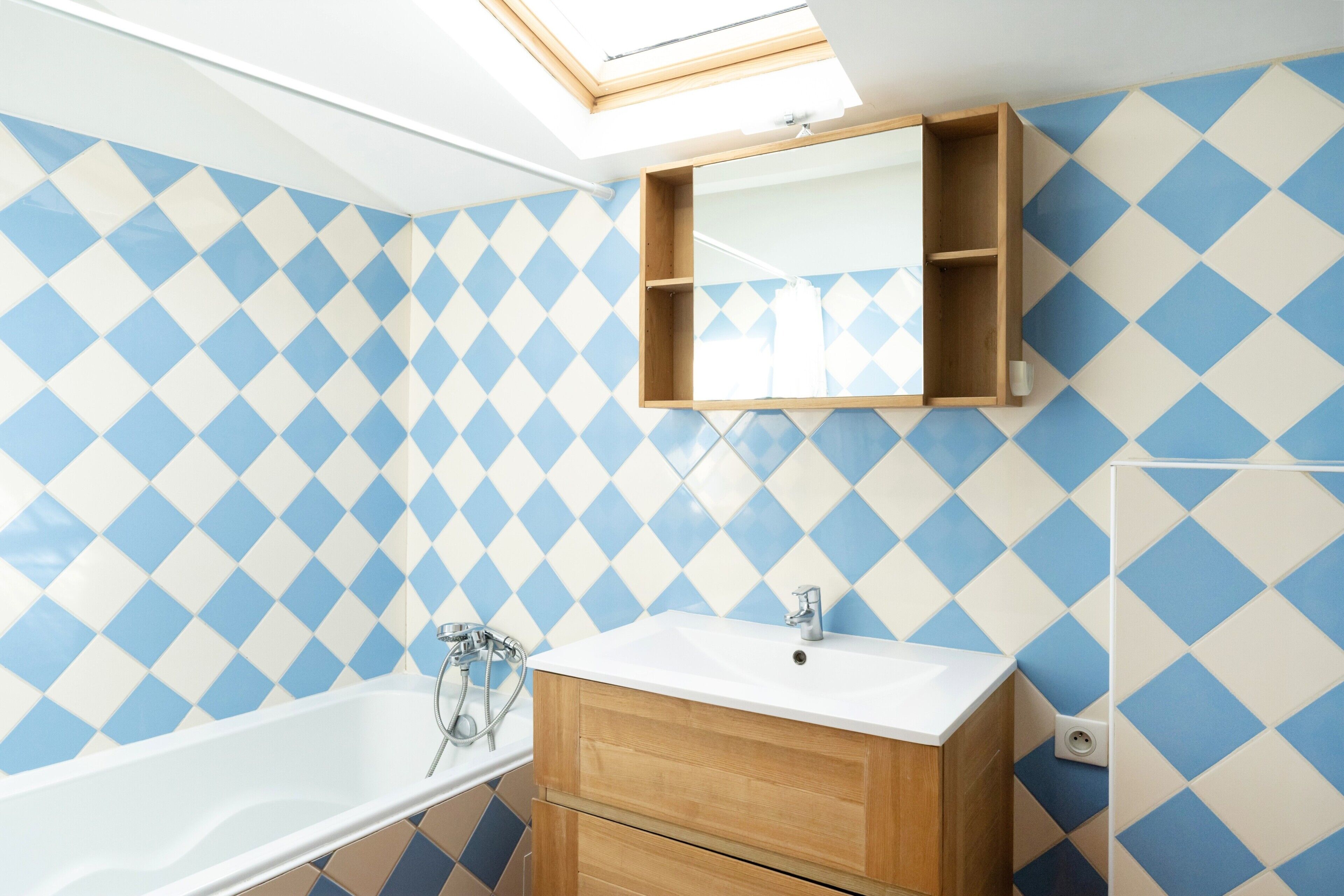 Une salle de bain avec un puits de lumière, une baignoire, un meuble-lavabo en bois et un miroir.