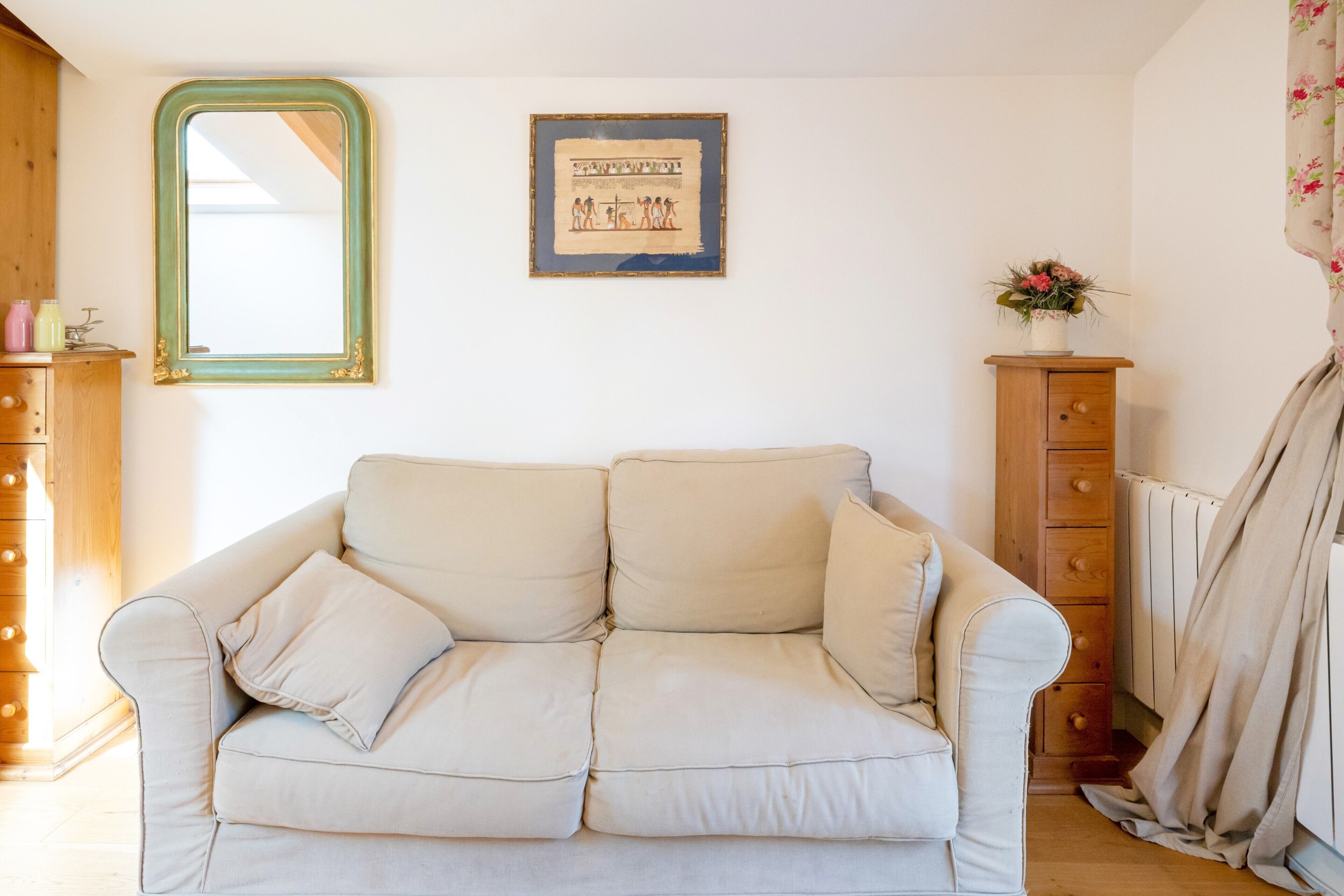 A beige sofa, a framed picture, a wooden cabinet, and a radiator.