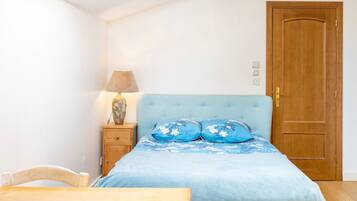 Een slaapkamer met een bed, een nachtkastje van hout, een lamp, een houten deur en een dakraam.