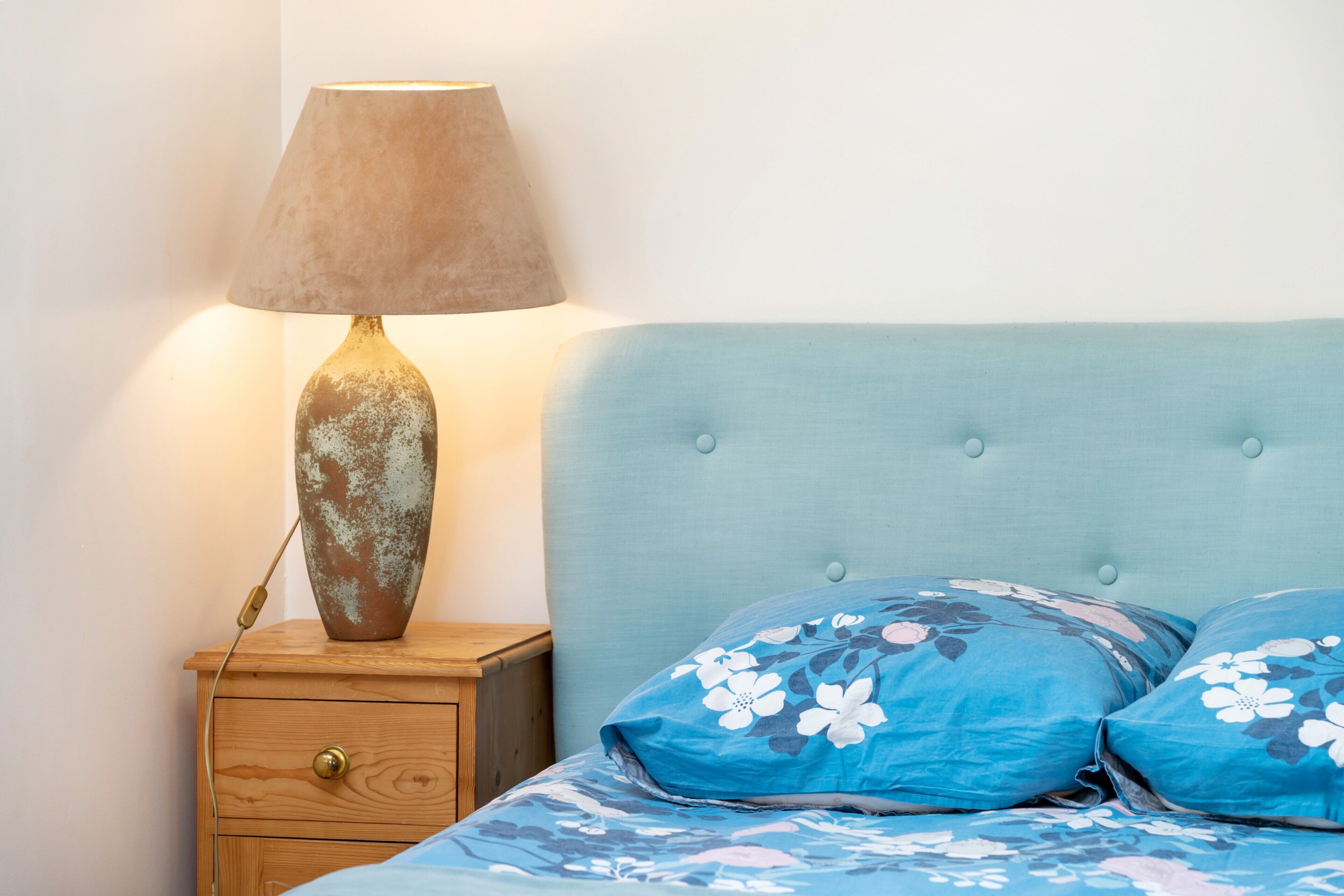 Un letto con biancheria da letto floreale, una testiera azzurra e una lampada su un comodino in legno.