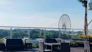 An outdoor seating area with tables and chairs, a view of a Ferris wheel, and a railing. - Modern Comfort in Pasay with Pool (Pasay)