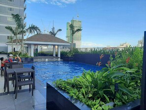 A rooftop pool with lounge chairs, surrounded by greenery and a view of a cityscape including a tall building under construction. - Modern Comfort in Pasay with Pool (Pasay)