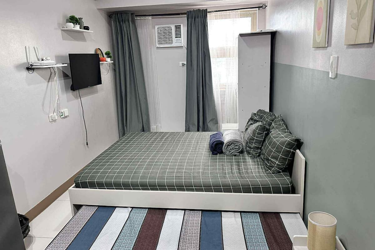 Une chambre à coucher avec un lit, une télévision, un miroir et une fenêtre avec des rideaux.