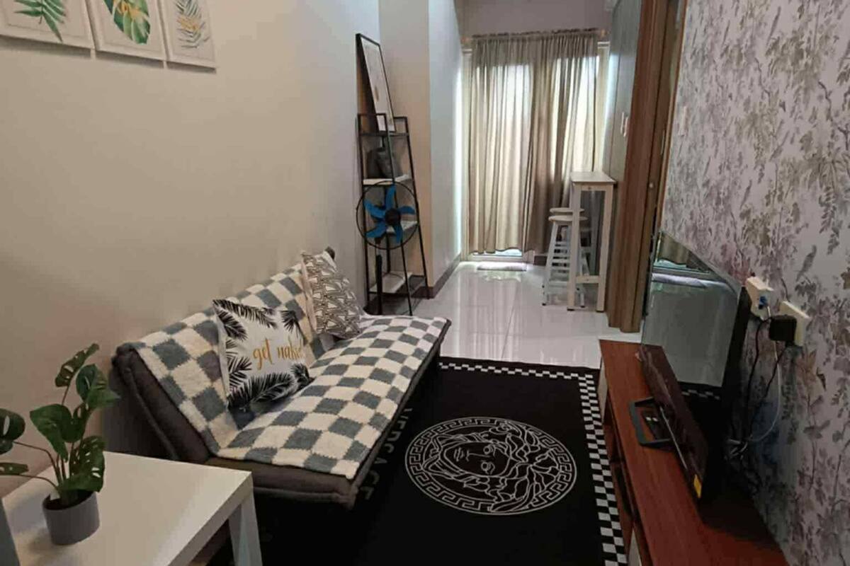 Un espace de vie compact comprenant un canapé, une petite table, un téléviseur et un tapis décoratif.